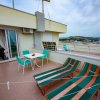 Terrazza con due sdraio a righe, un tavolo bianco e sedie verdi. Visuale della città.