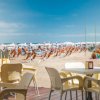 Tavoli e sedie di plastica su una terrazza con vista su una spiaggia con ombrelloni.