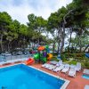 Piscina all'aperto con scivoli colorati e lettini sotto alberi.