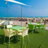 Tavoli e sedie verdi su prato sintetico vicino a spiaggia sabbiosa.