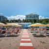 Spiaggia con ombrelloni gialli e lettini, accesso centrale con passerella rossa e bianca.