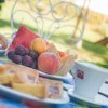Tavolo da colazione all'aperto con frutta, dolci e tazze di caffè su una tovaglia colorata.