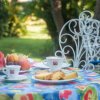 Tavolino all'aperto apparecchiato con colazione, frutta e caffè, sedie bianche decorative intorno.