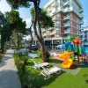Un hotel con parco giochi colorato, piscina e sedie a sdraio all'aperto, circondato da alberi.