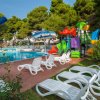 Area piscina con sdraio e ombrelloni, vicino a un parco giochi per bambini con scivoli colorati.