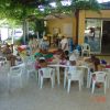 Bambini seduti a tavoli sotto un pergolato, impegnati in attività creative.
