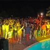 Festa serale all'aperto con molte persone che ballano accanto a una piscina.