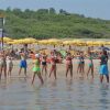 Persone in costume da bagno fanno aerobica in acqua vicino a ombrelloni gialli sulla spiaggia.