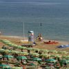 Spiaggia con ombrelloni verdi e gialli, lettini e alcune persone in riva al mare.